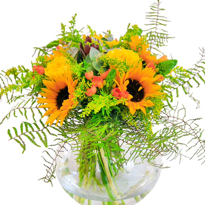 The first impression of this beautifully crafted bouquet is one of pure, sun-kissed exuberance-a joyful display that brings the warm, golden vibes of Balham's lively community into your space. Sunflowers shine in the heart of the arrangement, with velvety petals unfurled around deep, inviting centers that seem to soak up and reflect the glow of a summer afternoon. Blooming nearby, golden garden roses spiral elegantly, their rich layers and softly scented petals adding softness and sophistication reminiscent of fresh flower stalls at Balham Farmers' Market. Here and there, clusters of shining red Hypericum berries offer a perfect counterpoint, popping with vibrant color amid the lush backdrop of greens. Cascading fern fronds and wispy sprigs evoke the natural beauty of local parks and gardens, adding texture and depth, while the gentle presence of eucalyptus lends a contemporary, calming touch. The round, crystal-clear vase in which the bouquet sits magnifies every stem and swirl of water, creating a sense of freshness and meticulous craftsmanship you expect from Flowers Balham. Whether gracing a dinner table on Ramsden Road, brightening up a living room, or delivered as a heartfelt gesture, this arrangement embodies hope, community, and a cheerful embrace for every occasion.
