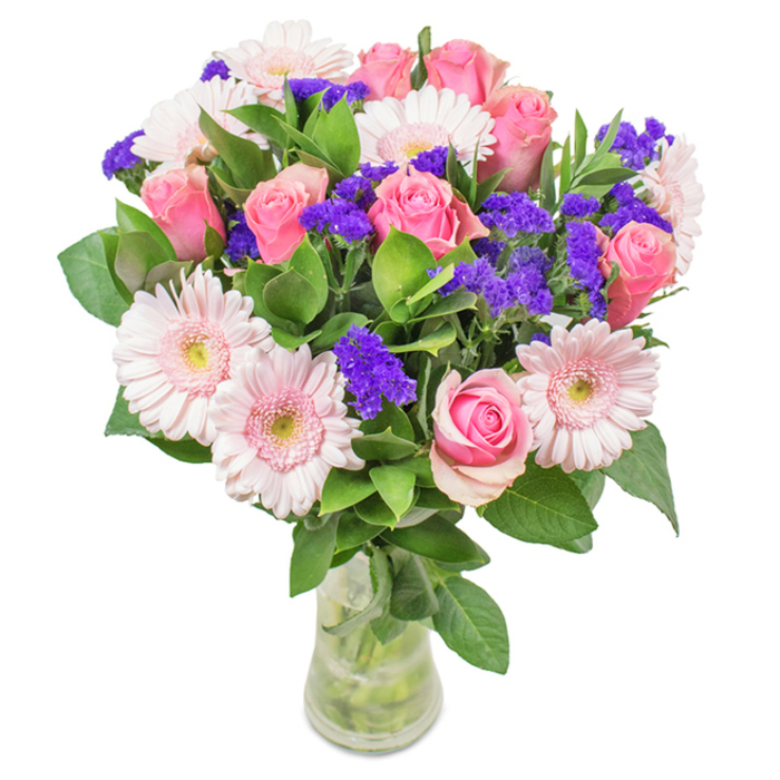 A refined floral arrangement crafted by Balham's local florists, showcased in a tall, elegant glass vase, with water glistening around neatly trimmed stems. Standing at the heart are about seven to nine pink roses-some in tight bud, others just beginning to unfurl-highlighting the timeless spiral of their petals. Around them, five to seven pale pink Gerbera daisies create a harmonious circle, recognizable by their broad, radiating petals and nearly white centres. Vivid clusters of purple statice or limonium provide striking texture, a signature touch seen at the bustling flower stalls along Balham High Road. Lush green foliage supports the bouquet, both framing and enhancing the vibrant colours above. With its inviting freshness and abundant look, this floral display is suitable for birthdays, anniversaries, Mother's Day, or as a beautiful accent for homes near Ritherdon Road. The entire composition encapsulates the spirit of joy, warmth, and sophistication that defines Balham.